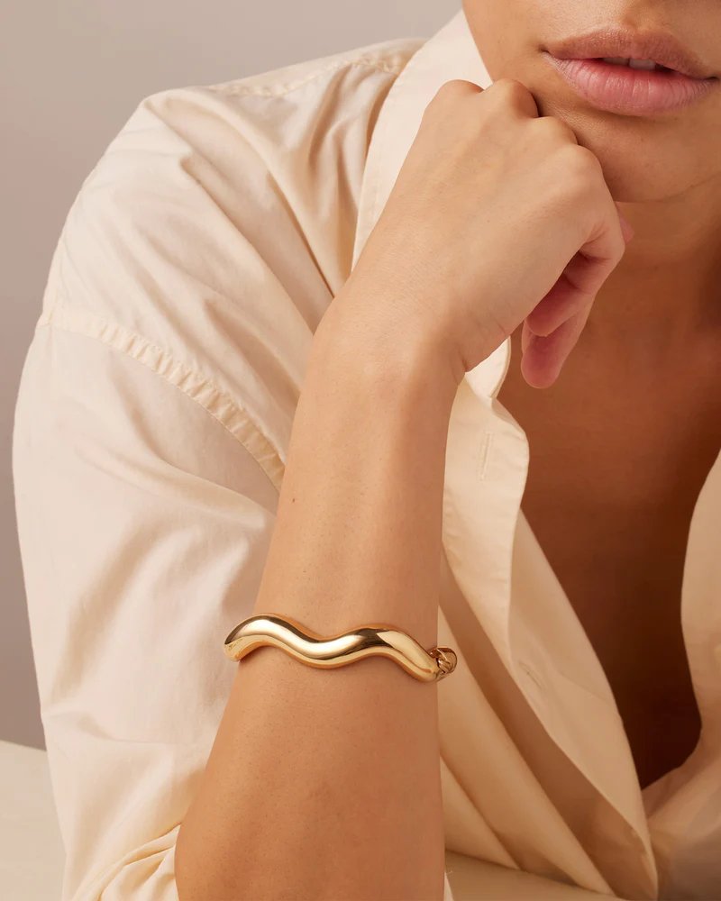 Jenny Bird Ola bangle in high polish gold. Curved gold bangle with a hinge and tab lock closure styled on model's arm.