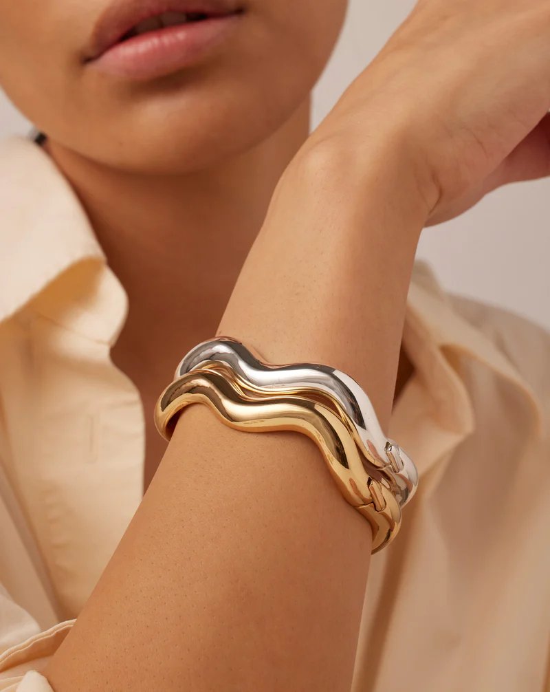 Jenny Bird Ola bangle in high polish gold. Curved gold bangle with a hinge and tab lock closure, styled as a stack of two on model's arm. 